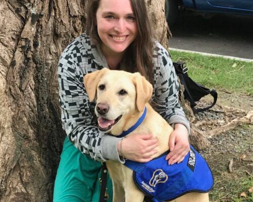 Helen Vivienne Fletcher sitting under a tree hugging her guide dog.