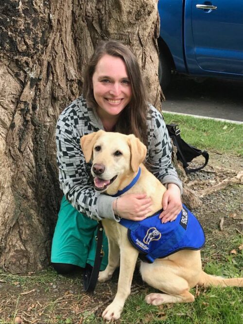 Helen Vivienne Fletcher sitting under a tree hugging her guide dog.